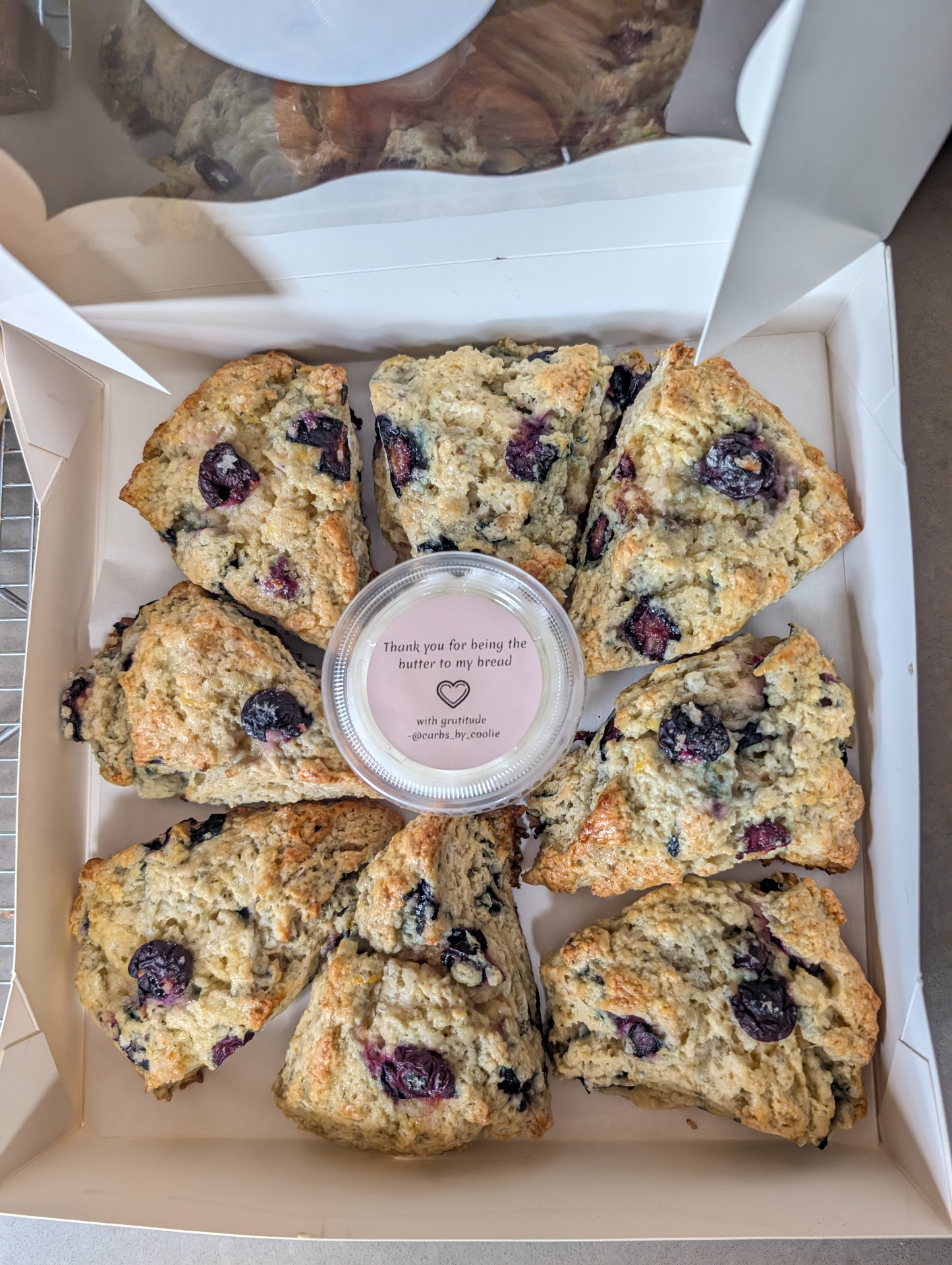 A white bakery box holding eight blueberry scones around a pot of butter