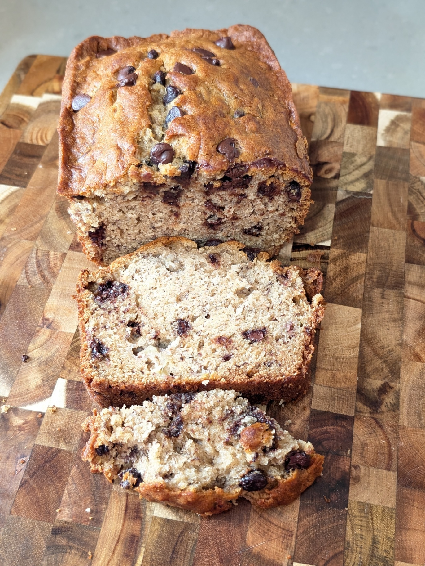Chocolate chip banana bread with one slice cut, on a wooden board